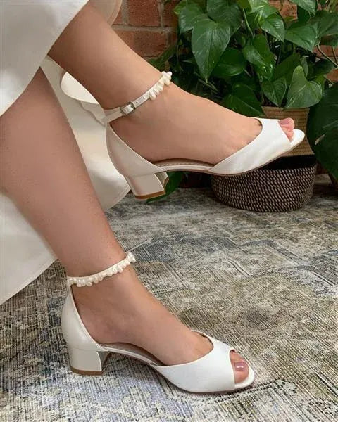 Zapatos de novia Fiona en satén marfil con puntera peep toe, sandalia tacón bajo de 3,8 cm y pulsera de perlas keshi para un look elegante y cómodo.